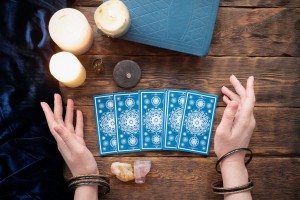 Fortune teller with tarot cards in the hand on brown table background.